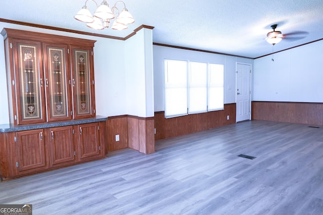 empty room featuring ceiling fan with notable chandelier, wood-type flooring, ornamental molding, and a textured ceiling