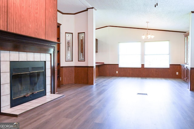 unfurnished living room with a chandelier, a textured ceiling, lofted ceiling, a fireplace, and ornamental molding