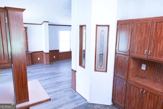 corridor featuring light wood-type flooring, a textured ceiling, ornamental molding, and wood walls