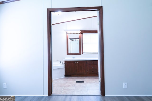 bathroom featuring wood-type flooring, vanity, vaulted ceiling, and tiled tub