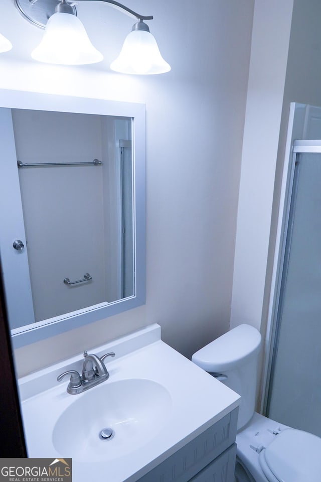 bathroom featuring a shower with door, vanity, and toilet