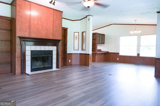 unfurnished living room featuring ceiling fan with notable chandelier, vaulted ceiling, a textured ceiling, and a tiled fireplace