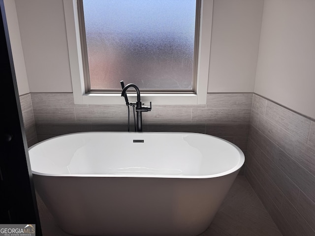 bathroom with a freestanding bath, tile walls, and a healthy amount of sunlight