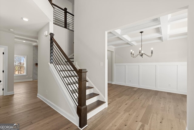 staircase with beam ceiling, coffered ceiling, an inviting chandelier, and wood finished floors