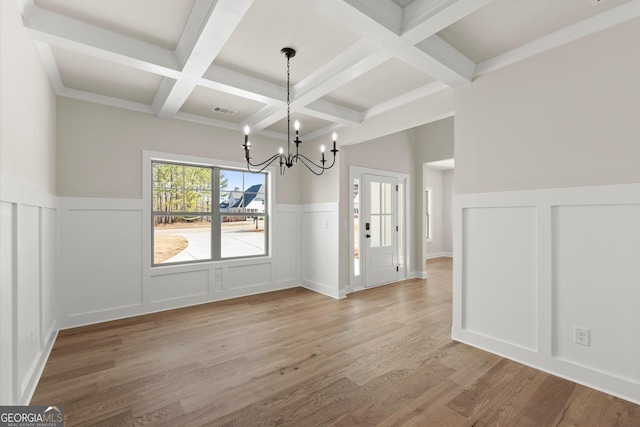 unfurnished dining area featuring visible vents, wainscoting, light wood-style floors, a chandelier, and beam ceiling