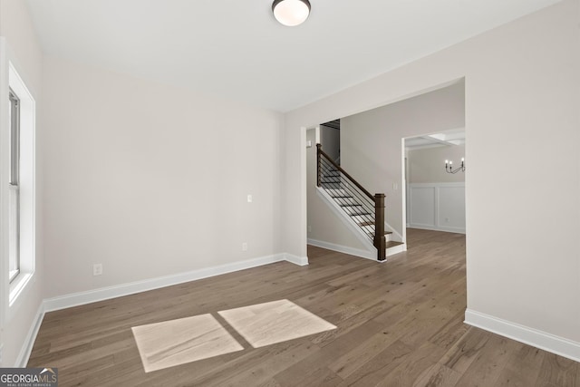 empty room featuring a chandelier, stairway, wood finished floors, and baseboards