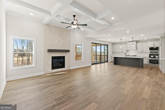 unfurnished living room featuring coffered ceiling, a fireplace, light wood-style flooring, and baseboards