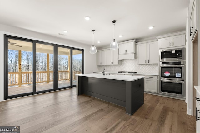 kitchen with tasteful backsplash, wood finished floors, built in microwave, light countertops, and stovetop