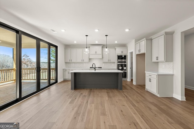 kitchen with a sink, light wood-style floors, light countertops, appliances with stainless steel finishes, and a center island with sink