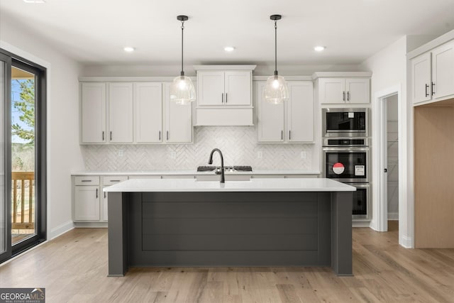 kitchen featuring light wood-style flooring, stainless steel appliances, a sink, light countertops, and an island with sink