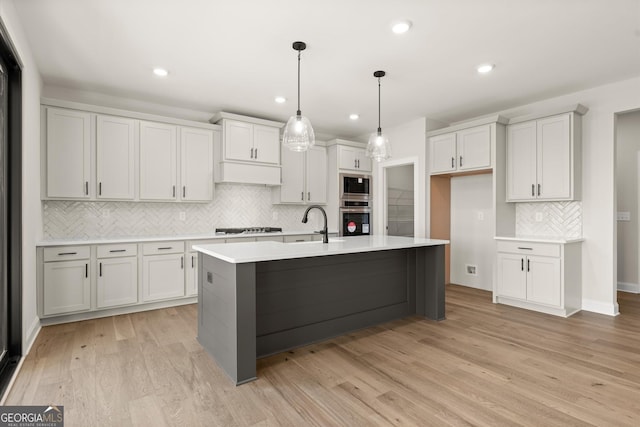 kitchen with light wood-style flooring, decorative light fixtures, light countertops, appliances with stainless steel finishes, and a center island with sink