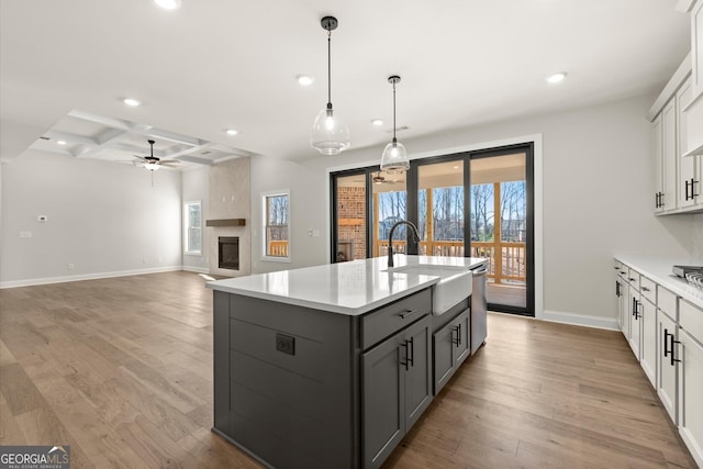 kitchen with gray cabinetry, coffered ceiling, a sink, light countertops, and light wood-type flooring