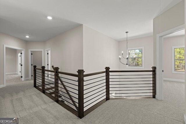 hall featuring an inviting chandelier, carpet flooring, and an upstairs landing