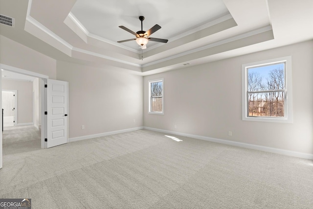 spare room featuring a tray ceiling, light carpet, visible vents, and baseboards