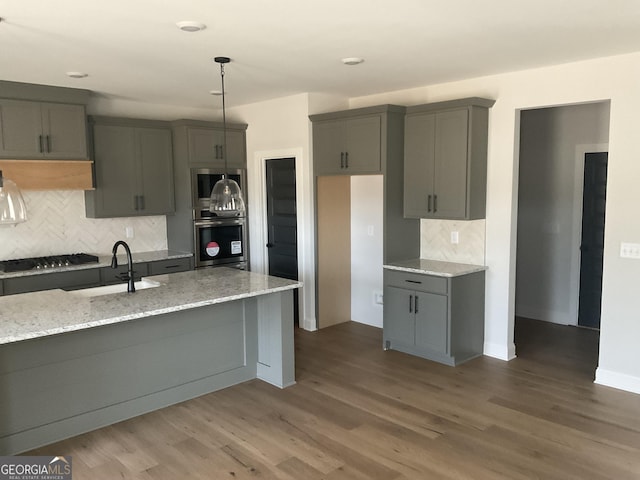 kitchen featuring gray cabinetry, stainless steel appliances, wood finished floors, a sink, and light stone countertops