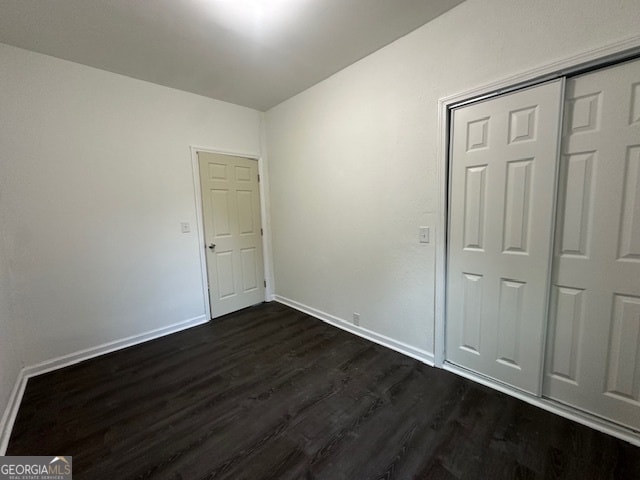 unfurnished bedroom with dark wood-type flooring and a closet