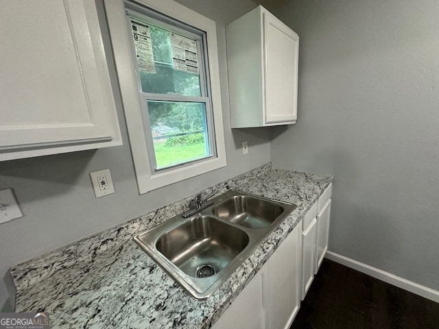 kitchen with light stone countertops, dark hardwood / wood-style floors, sink, and white cabinetry