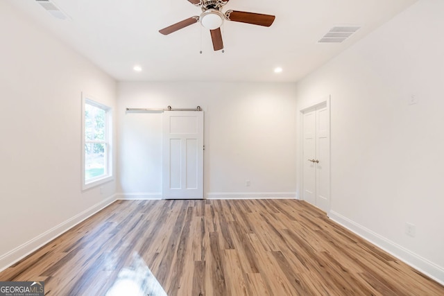 unfurnished bedroom with light wood-type flooring, ceiling fan, and a barn door