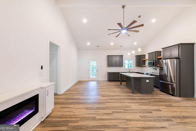 kitchen featuring light hardwood / wood-style flooring, stainless steel appliances, ceiling fan, high vaulted ceiling, and a kitchen island