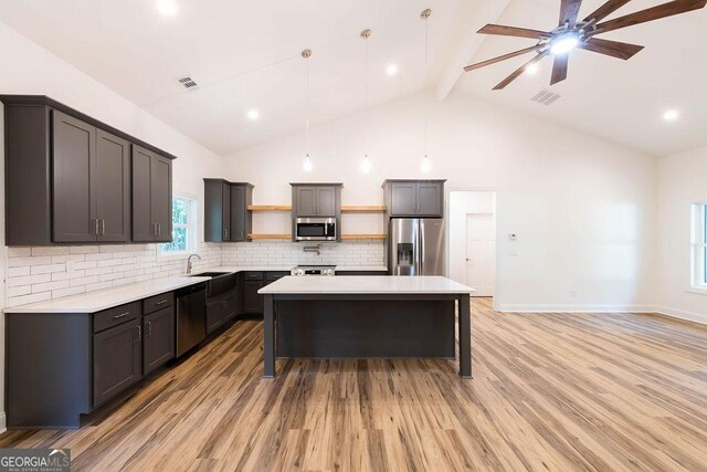 kitchen featuring a kitchen island, appliances with stainless steel finishes, decorative backsplash, ceiling fan, and light wood-type flooring