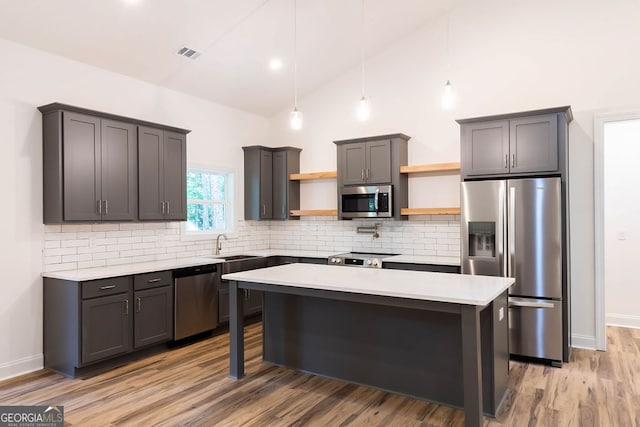 kitchen featuring backsplash, a center island, appliances with stainless steel finishes, gray cabinets, and wood-type flooring