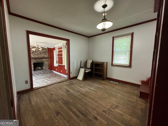 spare room with crown molding, dark hardwood / wood-style flooring, a fireplace, and brick wall