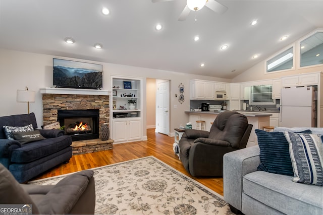 living room featuring a stone fireplace, vaulted ceiling, ceiling fan, built in shelves, and light hardwood / wood-style floors