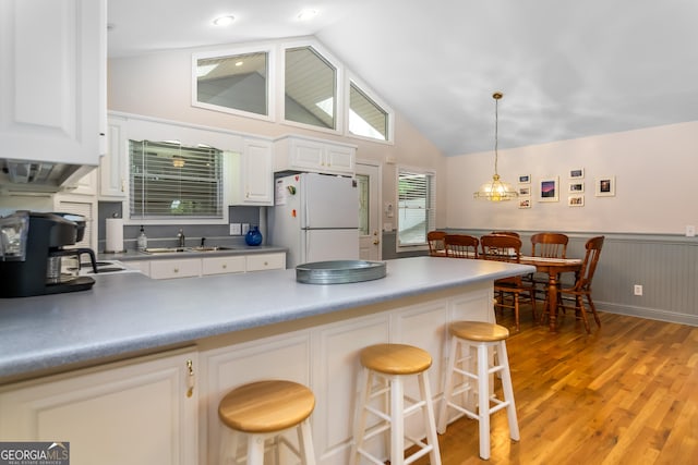 kitchen featuring white cabinets, a breakfast bar, white fridge, and pendant lighting