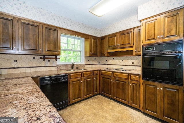 kitchen featuring black appliances, wallpapered walls, light stone counters, and a sink