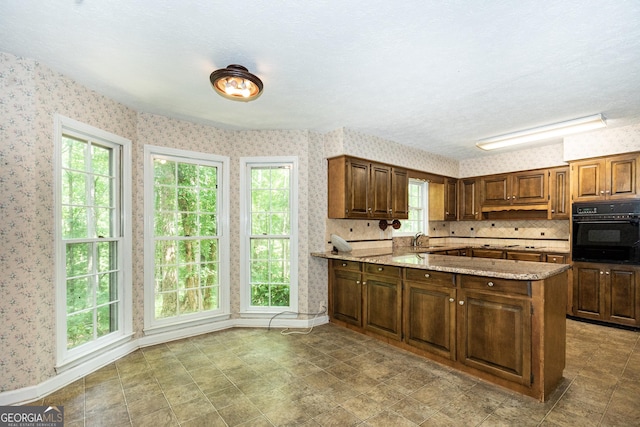 kitchen featuring black oven, a peninsula, a sink, and wallpapered walls