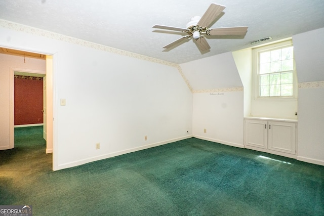 additional living space with a textured ceiling, dark colored carpet, vaulted ceiling, and ceiling fan