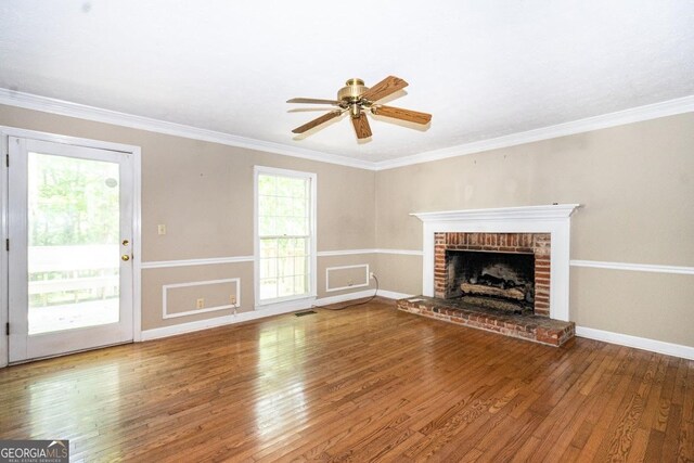 unfurnished living room with hardwood / wood-style floors, crown molding, a brick fireplace, and ceiling fan