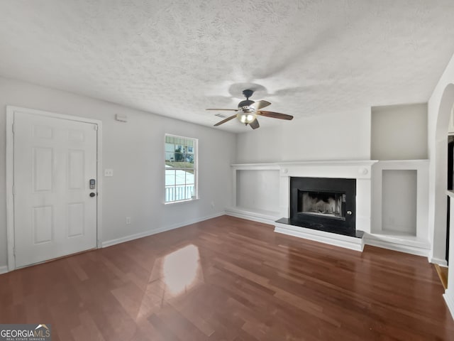 unfurnished living room with a textured ceiling, ceiling fan, and dark wood-type flooring