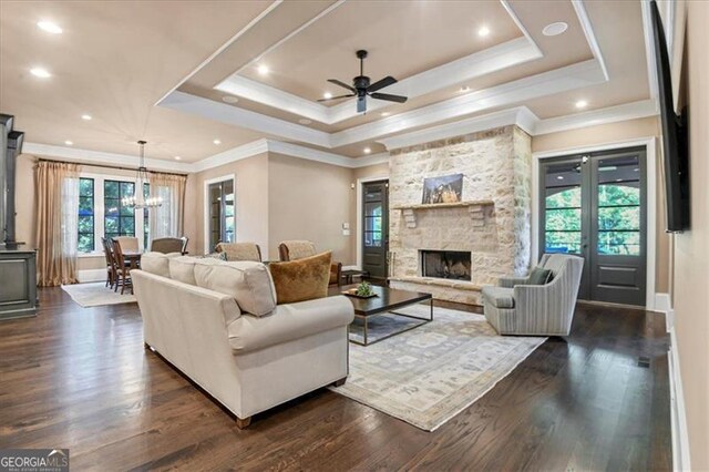 living room with a raised ceiling, crown molding, dark wood-type flooring, and a stone fireplace