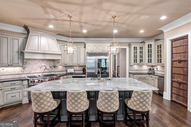 kitchen featuring dark stone countertops, dark hardwood / wood-style flooring, custom exhaust hood, a kitchen island with sink, and high end appliances