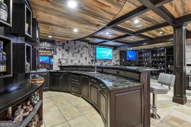 kitchen featuring decorative backsplash, an island with sink, light tile patterned floors, wooden ceiling, and dark stone countertops