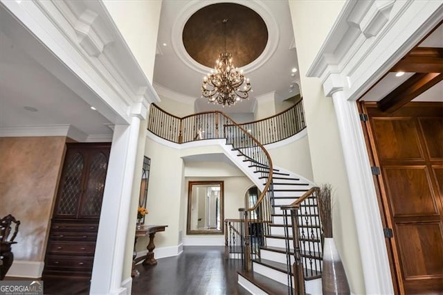 staircase with a high ceiling, wood-type flooring, ornamental molding, decorative columns, and a notable chandelier