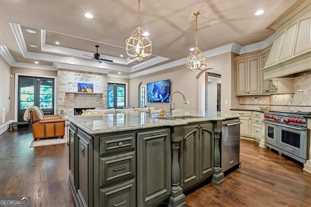 kitchen featuring stainless steel appliances, decorative backsplash, cream cabinetry, a fireplace, and a kitchen island with sink