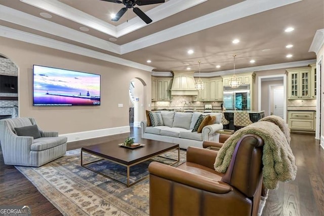 living room featuring ceiling fan, dark wood-type flooring, a raised ceiling, and crown molding