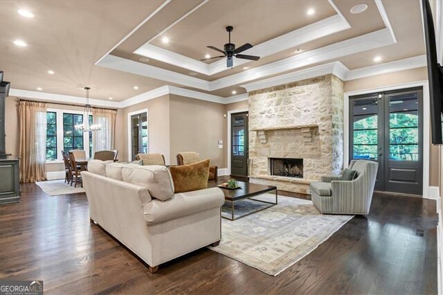 living room with crown molding, a raised ceiling, a healthy amount of sunlight, dark hardwood / wood-style flooring, and a stone fireplace