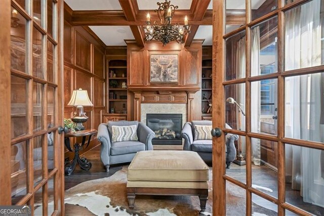 living area featuring hardwood / wood-style floors, a notable chandelier, built in shelves, beam ceiling, and coffered ceiling