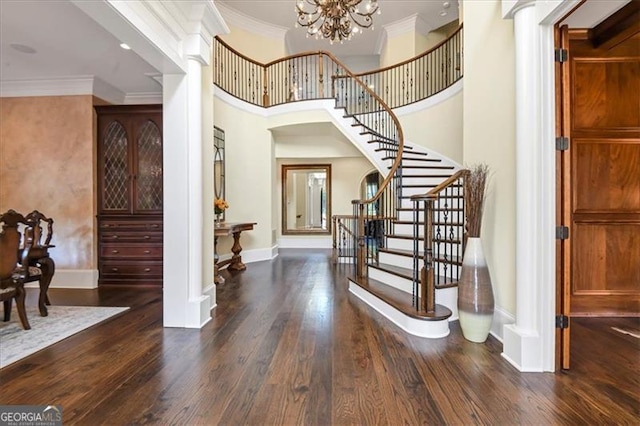 foyer entrance with dark hardwood / wood-style floors, a towering ceiling, decorative columns, an inviting chandelier, and crown molding