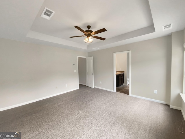 unfurnished living room featuring dark colored carpet, ceiling fan, and a raised ceiling