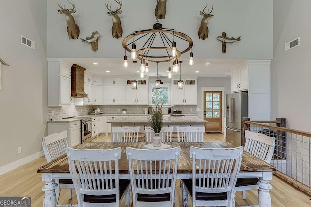 dining area with a notable chandelier, light wood-type flooring, and a towering ceiling