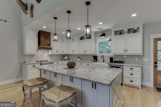 kitchen with white cabinets, premium range hood, light wood-type flooring, and a center island