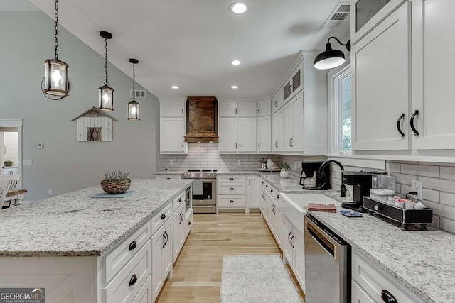 kitchen featuring custom range hood, appliances with stainless steel finishes, white cabinetry, a center island, and sink