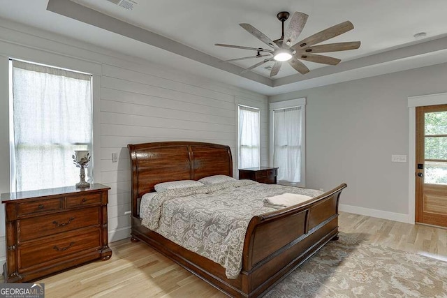 bedroom featuring ceiling fan, light wood-type flooring, and a tray ceiling