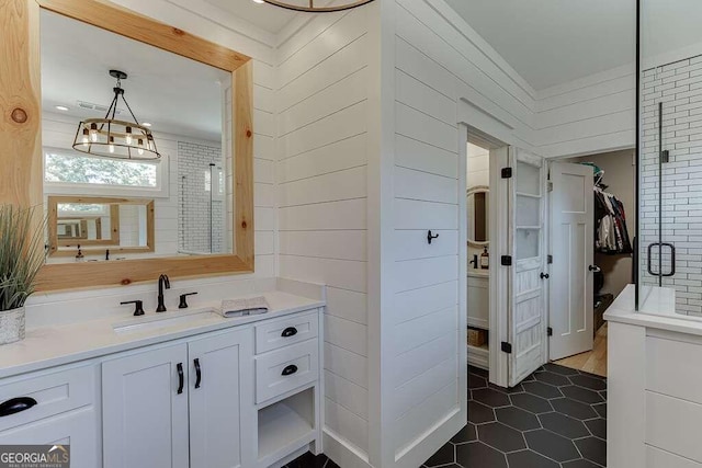 bathroom with an inviting chandelier, wooden walls, tile patterned floors, a shower with shower door, and vanity