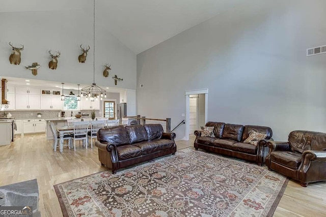 living room with light wood-type flooring, a notable chandelier, and high vaulted ceiling