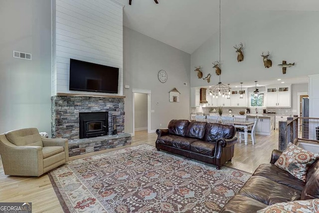 living room featuring sink, a stone fireplace, high vaulted ceiling, a notable chandelier, and light hardwood / wood-style floors